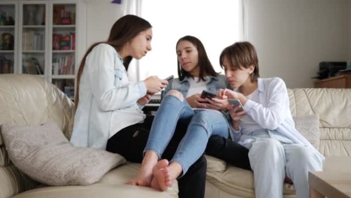 十几岁的女孩三胞胎姐妹在家看着坐在沙发上的社交媒体上的智能手机