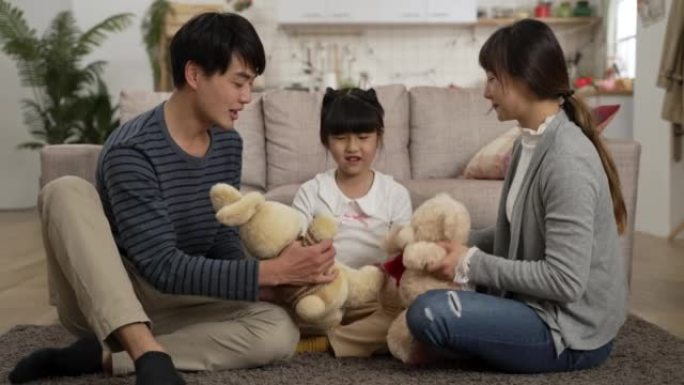 亚洲爸爸和妈妈在客厅里的地板上假装和他们的女学生玩得开心。他们抱着毛绒熊和兔子在家聊天