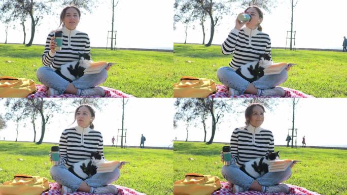 年轻女子坐在公园里，怀里抱着一只猫在喝咖啡