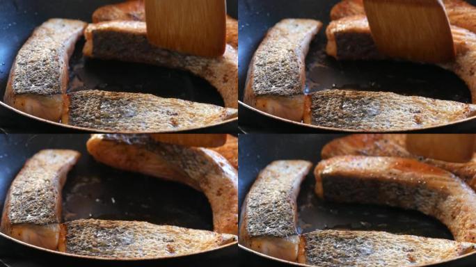 大块红鲑鱼鱼片在平底锅中油炸。木制厨房抹刀翻覆一片红鱼