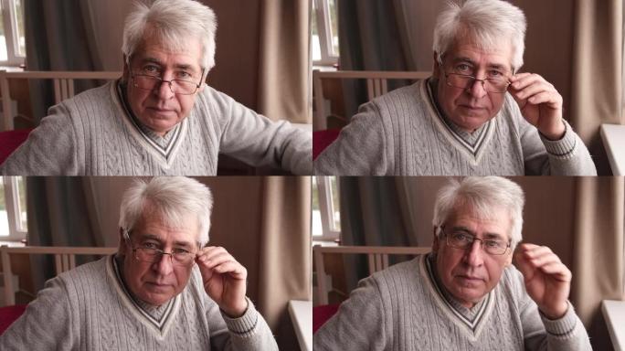 快乐的老人看着相机的特写肖像。高级白发男子。退休老人坐在家里靠近窗户。积极自信的老年人享受退休生活。