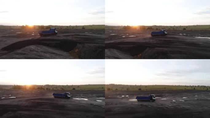 一辆强大的自卸车在夕阳下越野行驶。带有五个轮轴的卡车从容地克服了带有坑和水坑的困难地形