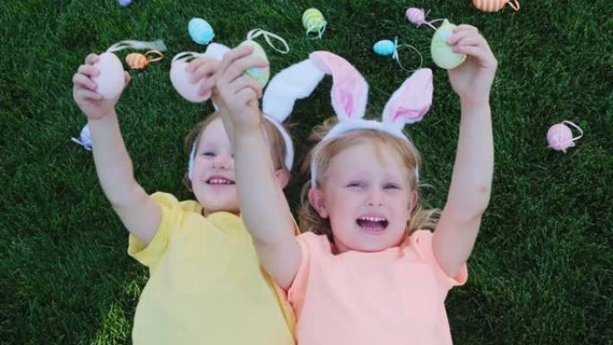快乐的小女孩，姐妹们在草地上玩得开心，用彩色复活节彩蛋闭上眼睛。