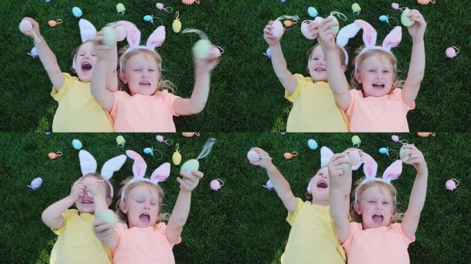 快乐的小女孩，姐妹们在草地上玩得开心，用彩色复活节彩蛋闭上眼睛。