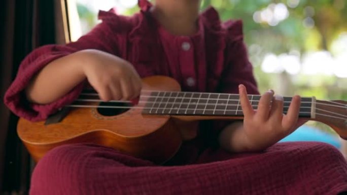 穿着红色连衣裙的小女孩在室内玩夏威夷四弦琴。