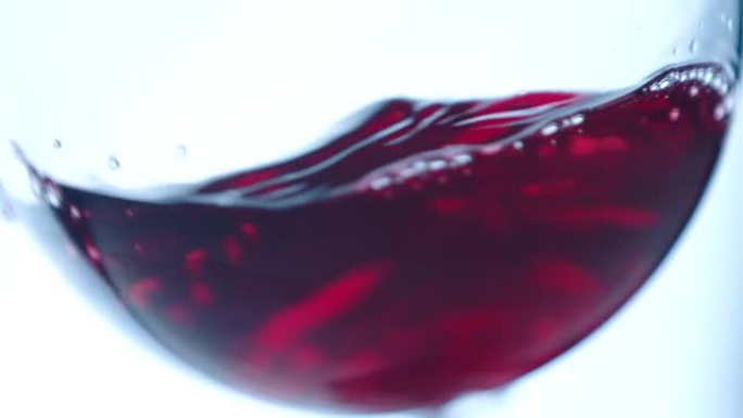 在散焦背景上在玻璃杯中挥舞红酒。美丽的葡萄酒广告素材。高脚杯内葡萄酒混合过程的特写视频。慢动作在阿瑞