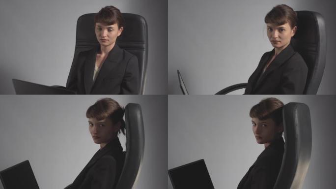 年轻严肃的女商人，笔记本电脑在办公椅上旋转，看着相机