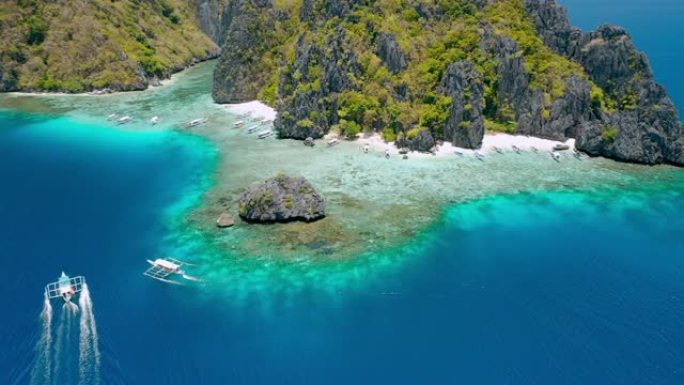 旅游banca船接近菲律宾巴拉望爱妮岛清水岛海滩的空中无人机镜头。岛前的岩石和清澈的浅绿松石泻湖水