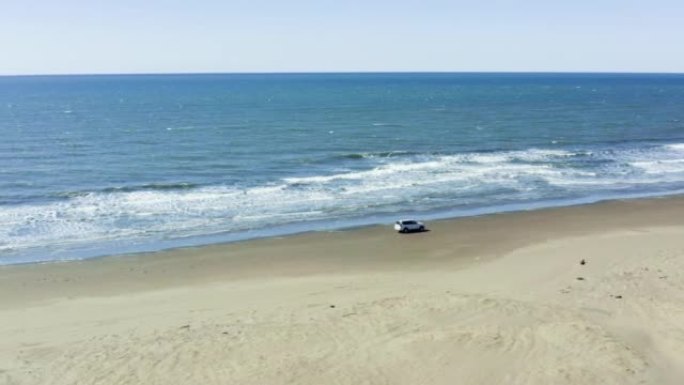 汽车在夏日沿着沙滩沙滩行驶，穿过河流和海浪中的白色泡沫。游客乘车旅行，并在相机上拍摄他们的假期和美丽