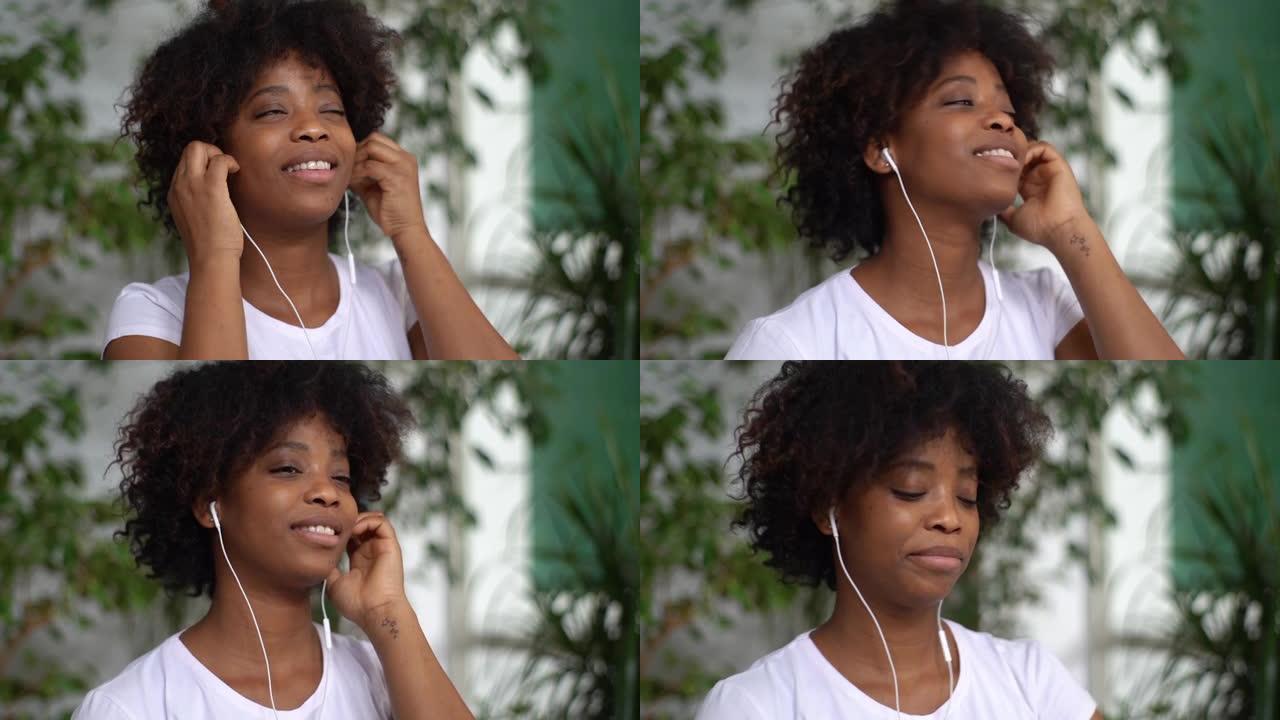 开朗的非洲年轻女子的特写脸戴上耳机，开始在绿色植物的灯光室里听最喜欢的音乐。
