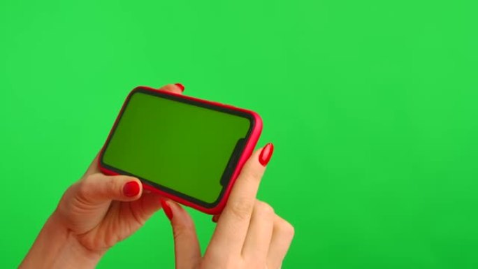 女性手持水平位置的绿色背景上带有工作区模拟屏幕的手机。女人触摸屏幕，点击并浏览互联网上的内容。广告区