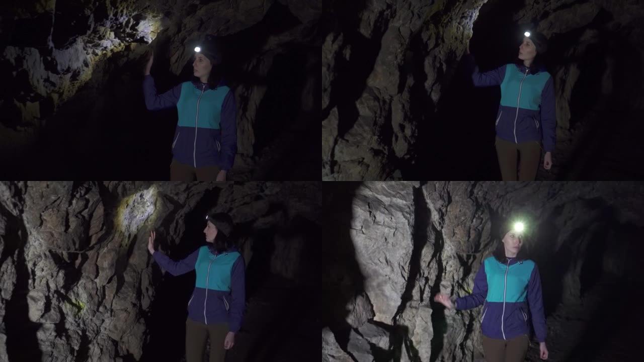 背着背包的肖像女孩旅行者在一个山洞里，额头上有手电筒，检查石头