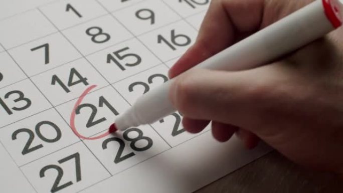 人的手用红笔在纸质日历上写下第21天。