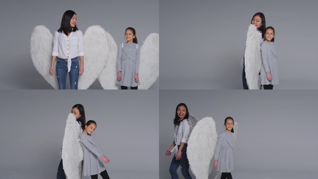 工作室背靠背拍摄微笑的女人和戴着天使翅膀的女孩