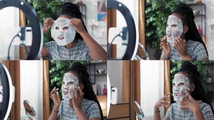 美容博主正在直播社交媒体上的化妆品化妆品，同时将织物美容面膜涂在脸上。Influencer在三脚架和