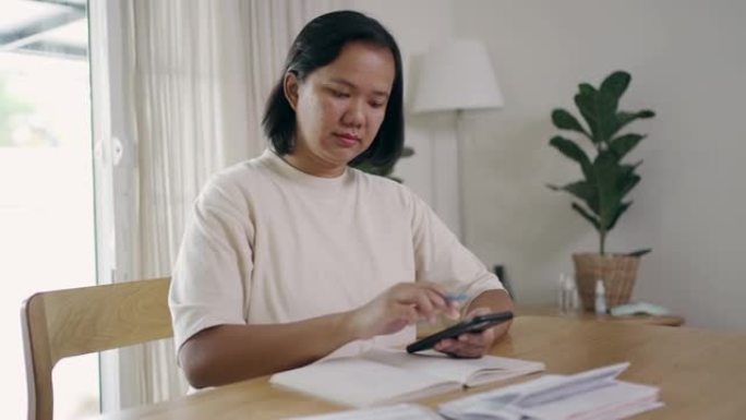 亚洲女子用手机做财务计算并记笔记