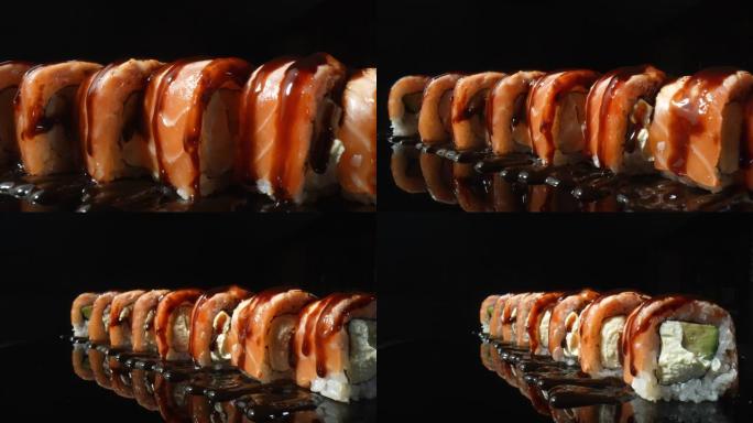 费城寿司卷配unagi酱，在黑色背景上旋转特写。寿司卷配三文鱼、米饭、鳄梨和奶酪。传统的日本料理搭配