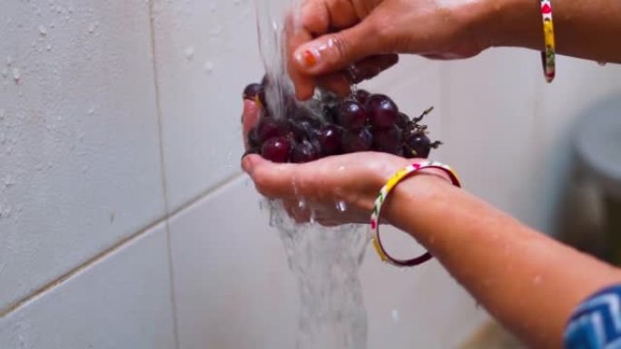 印度女性双手在家里水龙头的水流下洗葡萄果实的特写镜头。洗水果和蔬菜，保健。