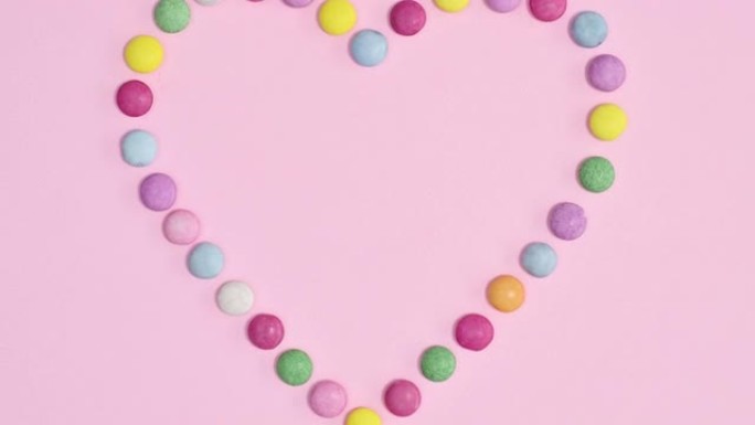 由鲜艳的粉红色背景上的彩色彩虹糖果制成的创意心形。停止运动