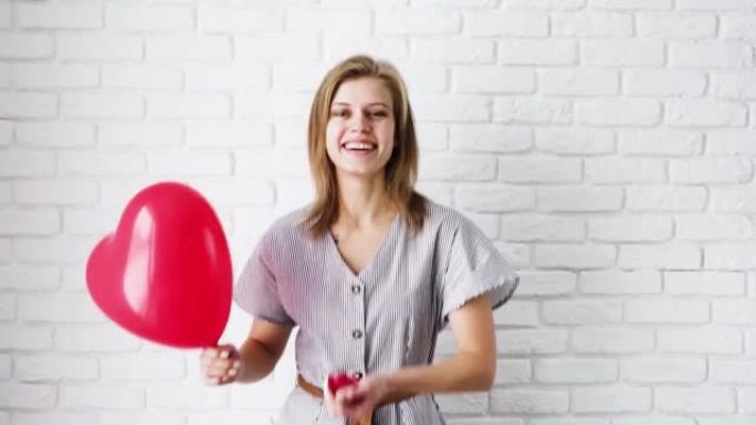 年轻的金发女子带着红色气球跳舞，扔红色心形五彩纸屑庆祝节日