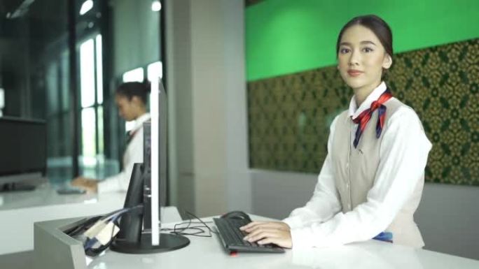 微笑的地勤人员在计算机显示器上工作并看着相机的肖像