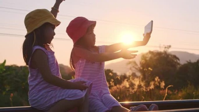 两姐妹坐在铁轨上，在日落时用智能手机自拍。亚洲姐妹喜欢一起度假。