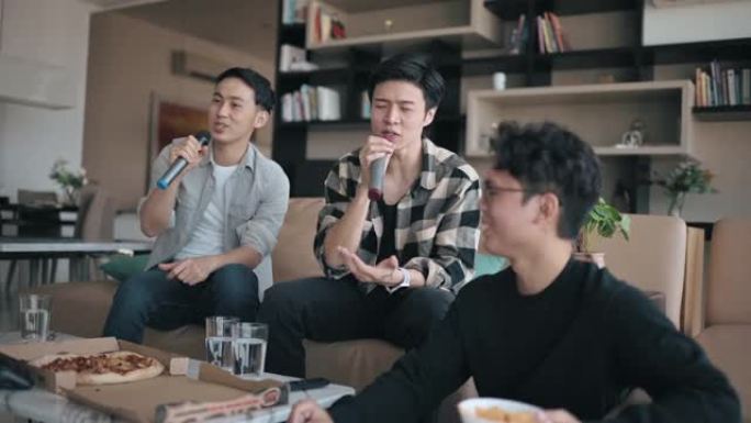 亚洲中国男性朋友周末在家吃披萨享受卡拉ok