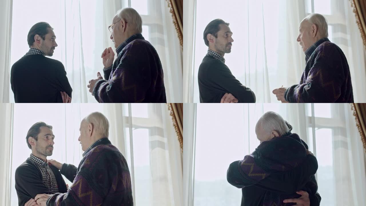 一名焦急的男子站在窗边凝视着窗外，他意识到身后有一位老人，于是转身拥抱了一下