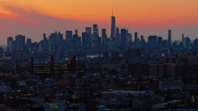 曼哈顿市中心和自由塔在夜晚照亮。日落时分，布鲁克林住宅区的远处景色，天空充满戏剧性。航拍镜头的移动速