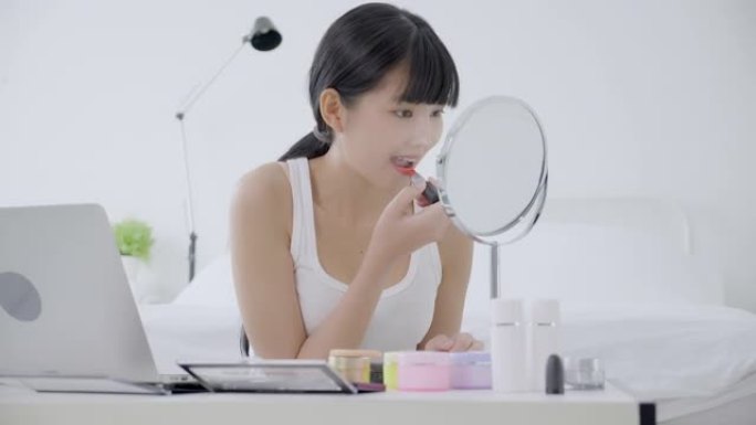 年轻的亚洲女性的美丽，用口红在嘴上学习化妆，在线观看笔记本电脑教程，女性教学，并在流媒体上讲解化妆。