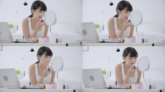 年轻的亚洲女性的美丽，用口红在嘴上学习化妆，在线观看笔记本电脑教程，女性教学，并在流媒体上讲解化妆。