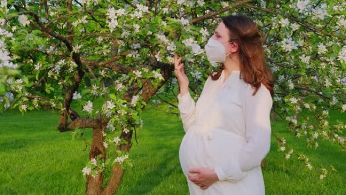孕妇在医用面膜n95与苹果树花在春天的自然。2019冠状病毒病流行期间幸福怀孕，冠状病毒大流行隔离
