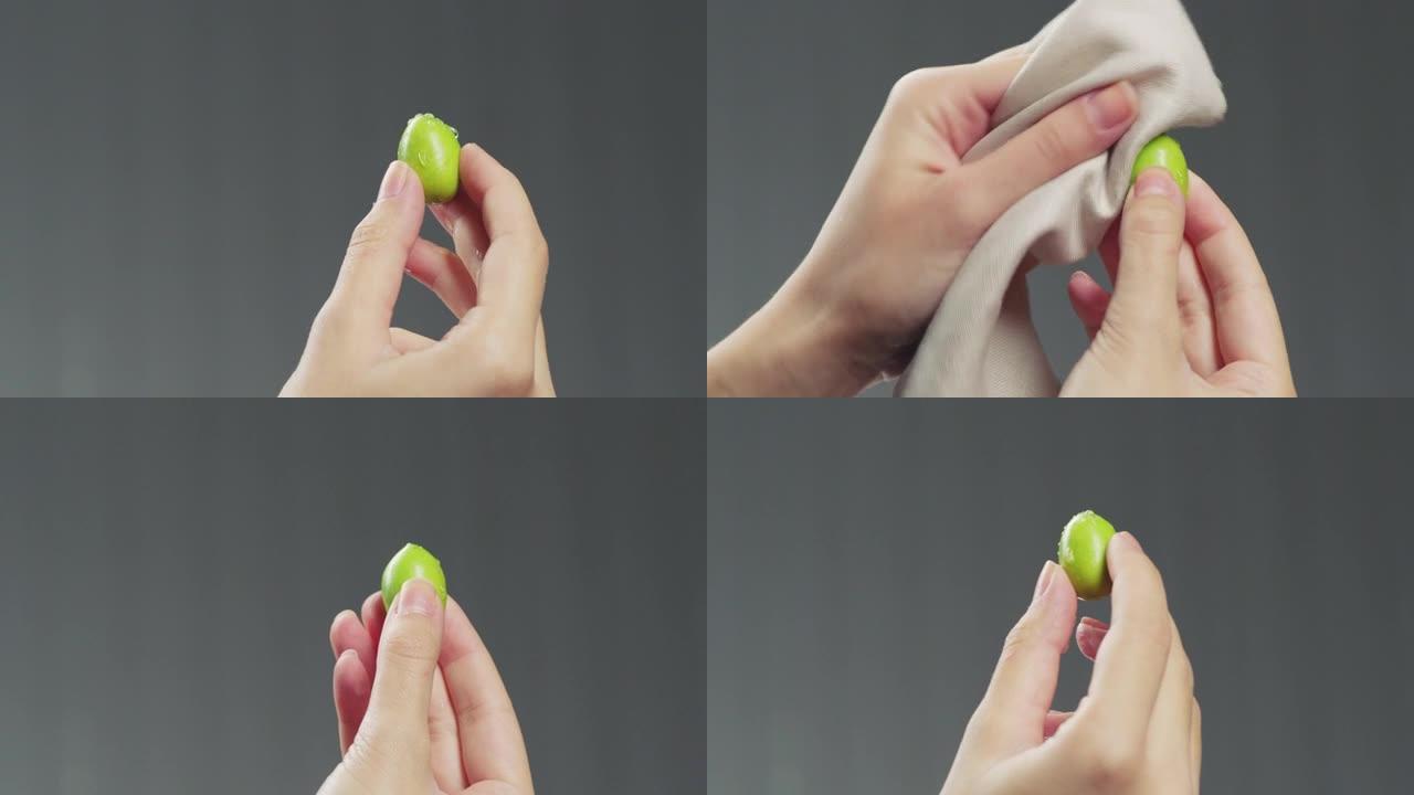 一只绿色的橄榄和一只雄性的手。手在擦一只橄榄。