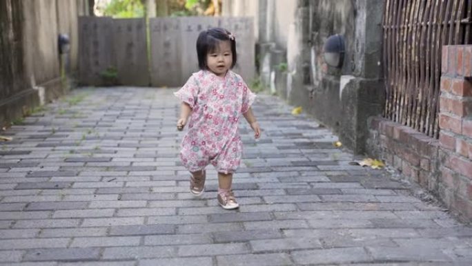 穿着和服的好奇的日本蹒跚学步的女孩在玩耍时蹒跚学步地走在砖砌的人行道中间。