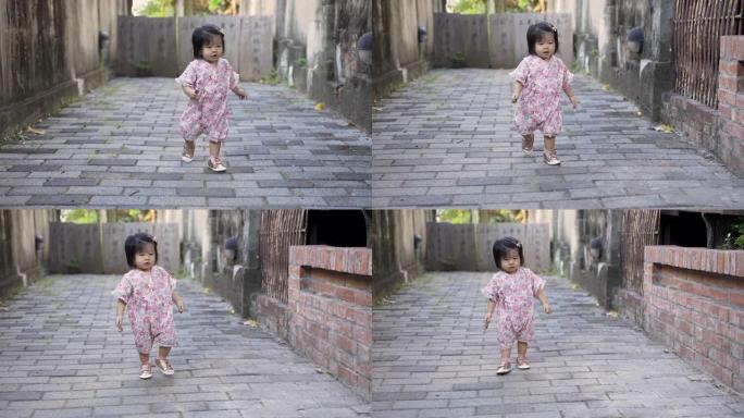 穿着和服的好奇的日本蹒跚学步的女孩在玩耍时蹒跚学步地走在砖砌的人行道中间。