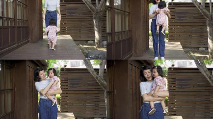 穿着和服的慢动作日本蹒跚学步的女孩正沿着她家的室外走廊蹒跚地走向微笑的母亲，母亲弯腰抬起她。