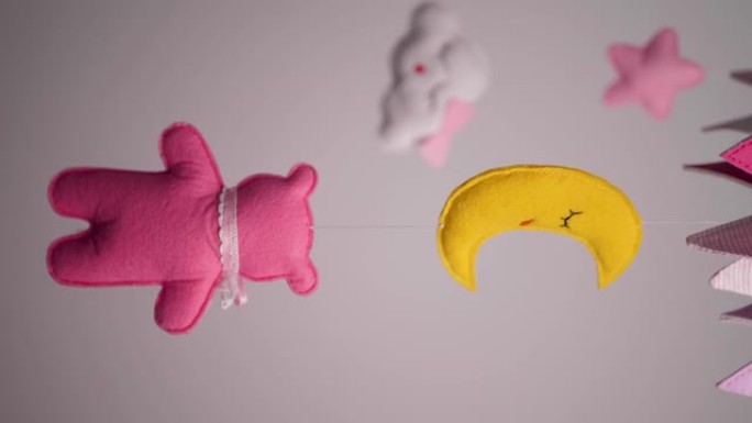 婴儿手机，带有粉红色手工缝制的动物和鸟类玩具，白色墙壁背景上有黄色的月亮。