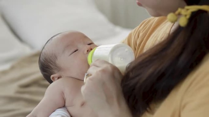 4k，一个2个月大的亚洲新生男孩正在母亲腿上的瓶子里睡觉和哺乳，母亲的手握着瓶子。