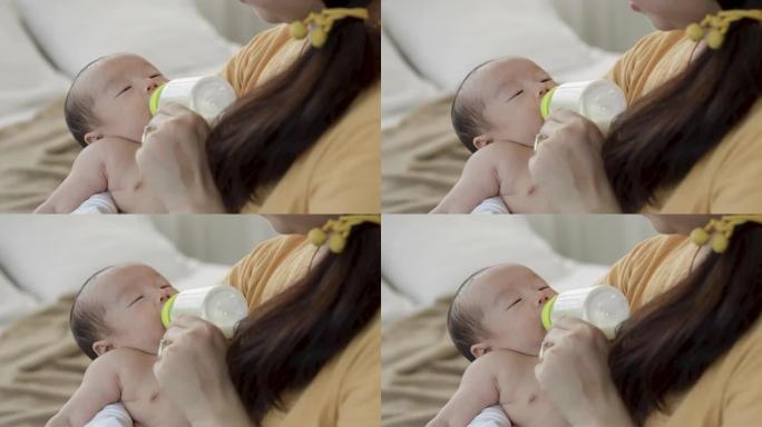 4k，一个2个月大的亚洲新生男孩正在母亲腿上的瓶子里睡觉和哺乳，母亲的手握着瓶子。