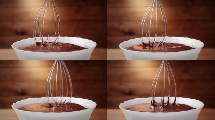 在厨房中将融化的液体巧克力与钢搅拌器近距离混合。热巧克力混合漩涡和滴在木制背景的白色碗。烹饪手工巧克