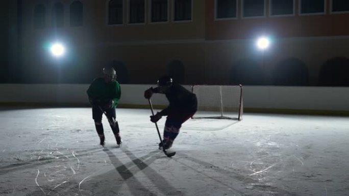 两名身穿制服和头盔的男子在冰场上滑冰，击中冰球并相互碰撞。职业曲棍球运动员在带有聚光灯的黑暗溜冰场上