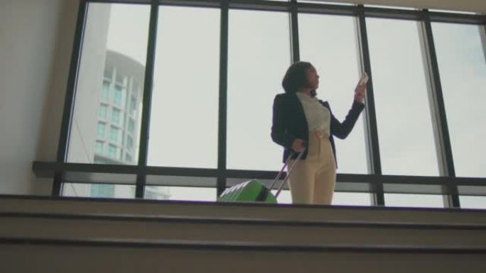 在机场窗户附近使用智能手机站立的带手提箱的女商人的4k录像