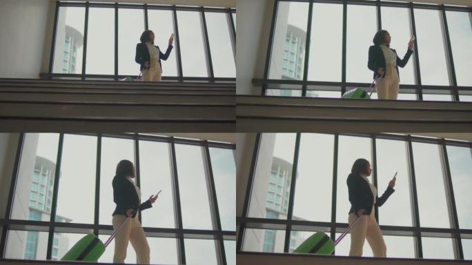 在机场窗户附近使用智能手机站立的带手提箱的女商人的4k录像