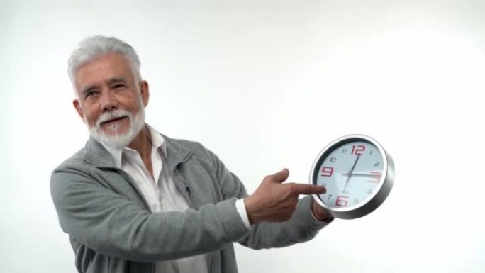 一位白人时尚老人的肖像指向时钟概念时间就是金钱。在白色背景的工作室里。趋势老化的概念。