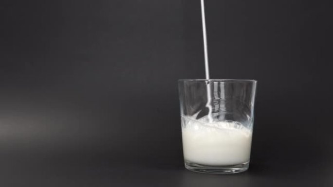 一个人的手拿着一盒美味的鲜牛奶，然后将其倒入玻璃杯中，直到到达顶部。