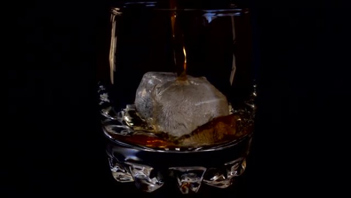 在孤立的黑色背景上将威士忌倒入加冰的玻璃杯中。慢动作。