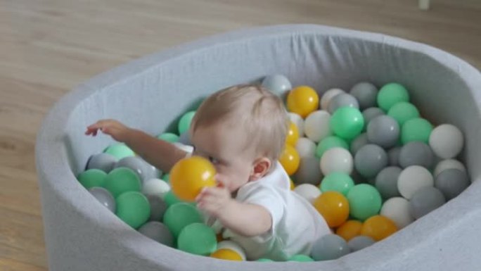 孩子在家打球。快乐的孩子在软球坑里，有五颜六色的球给幼儿，高加索男婴在家里玩得开心。
