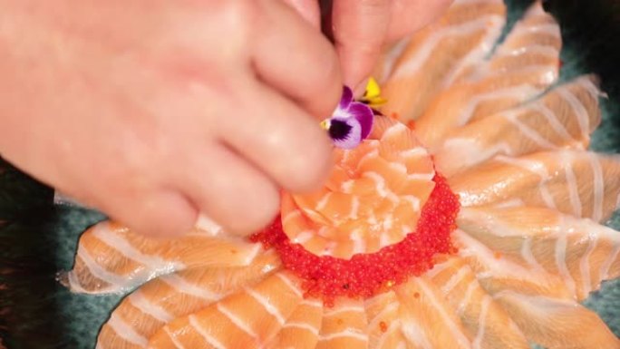 食物电镀-将鲜花放在生鱼片鲑鱼玫瑰上的厨师。