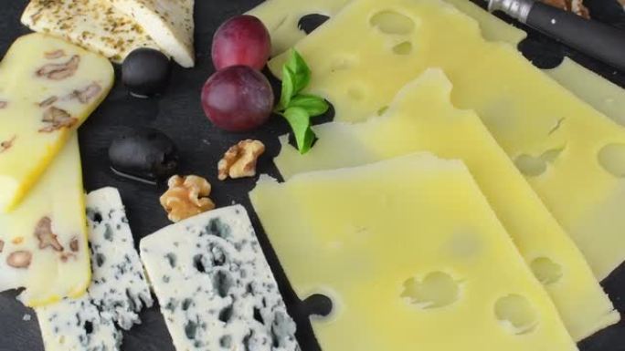 奶酪拼盘搭配各种奶酪，葡萄，黑色背景上的坚果。意大利奶酪和水果拼盘在石板旋转背景上。