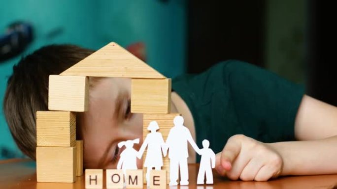 肖像快乐的高加索孩子扮演剪纸家庭，用木制立方体建造房屋。这个男孩梦想着一个家庭和一个家。玩积木的孩子